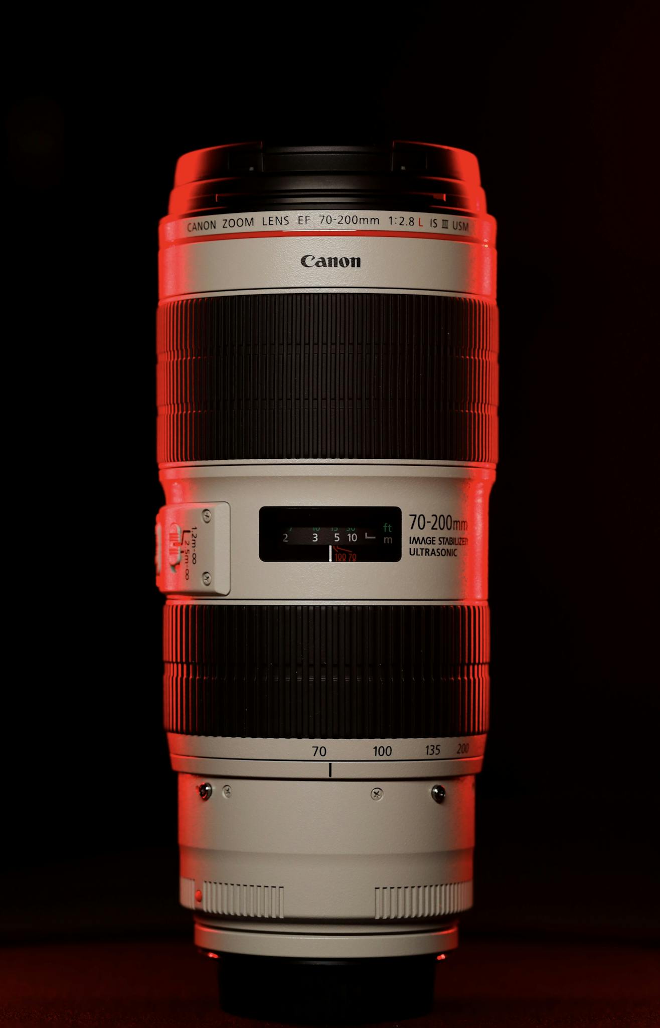 Close-up of a Canon 70-200mm zoom lens with dramatic red studio lighting.
