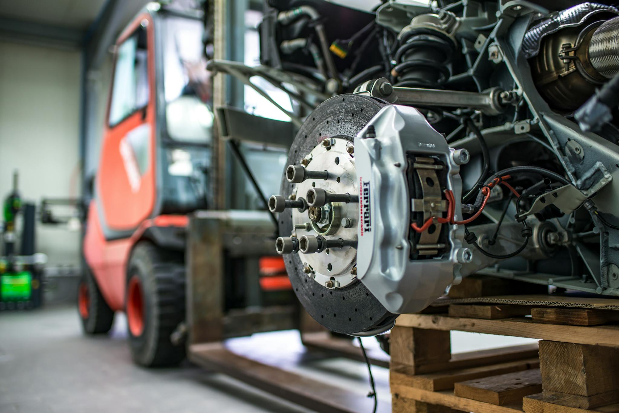 Detailed view of an automotive brake caliper and disc in an industrial workshop setting.